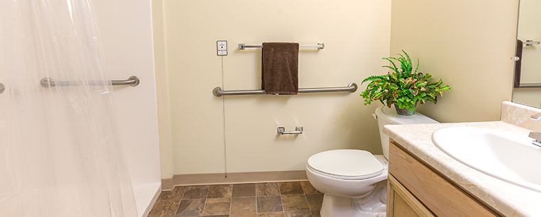 A bathroom with a toilet, towel rack, grab bar, and tiled floor.