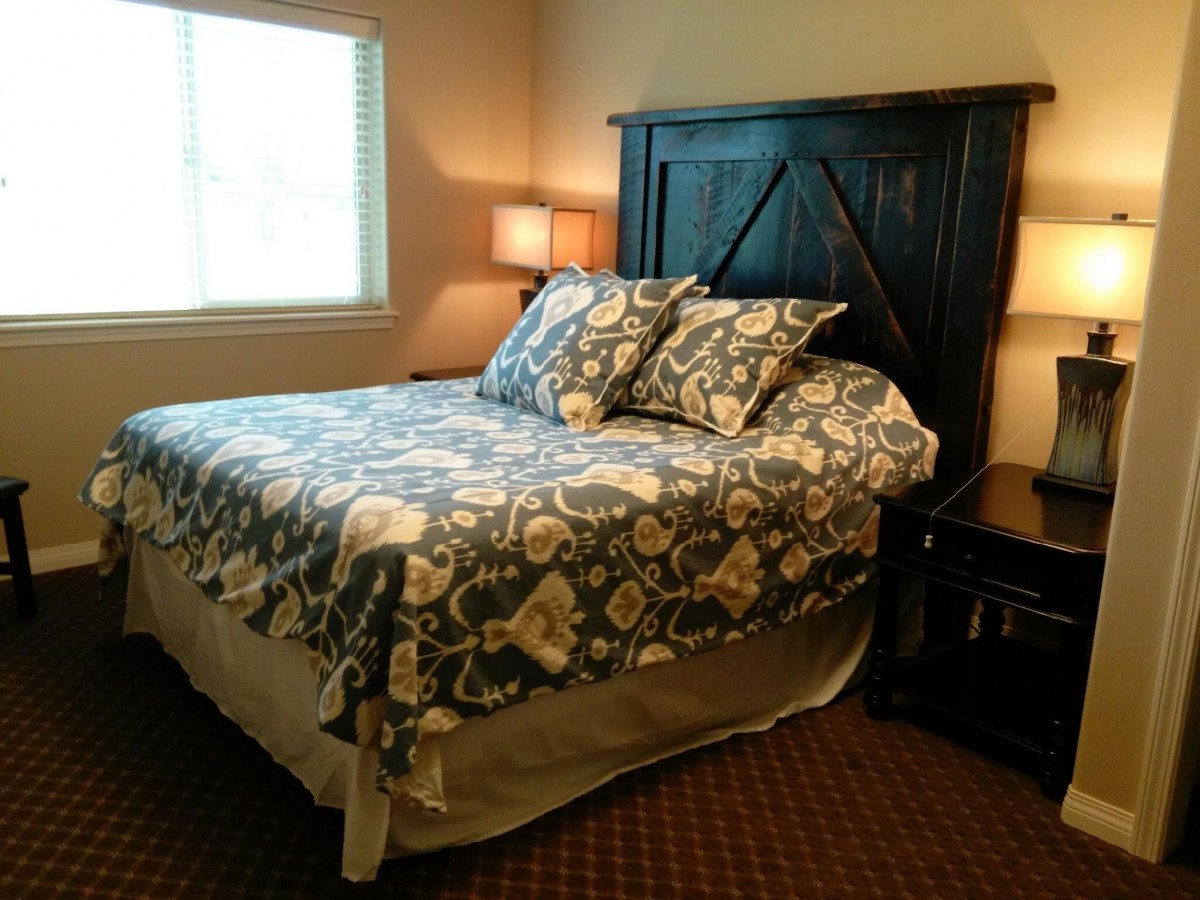 A cozy bedroom with a neatly made bed and patterned bedding, illuminated by table lamps.