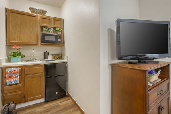 A compact kitchen area with wooden cabinets, a microwave, and a television on a separate stand.