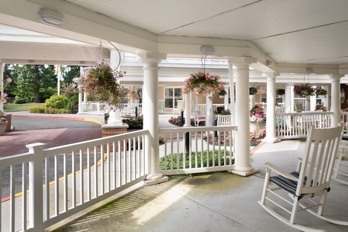 A cozy porch with white columns and hanging plants, basking in the sunlight.