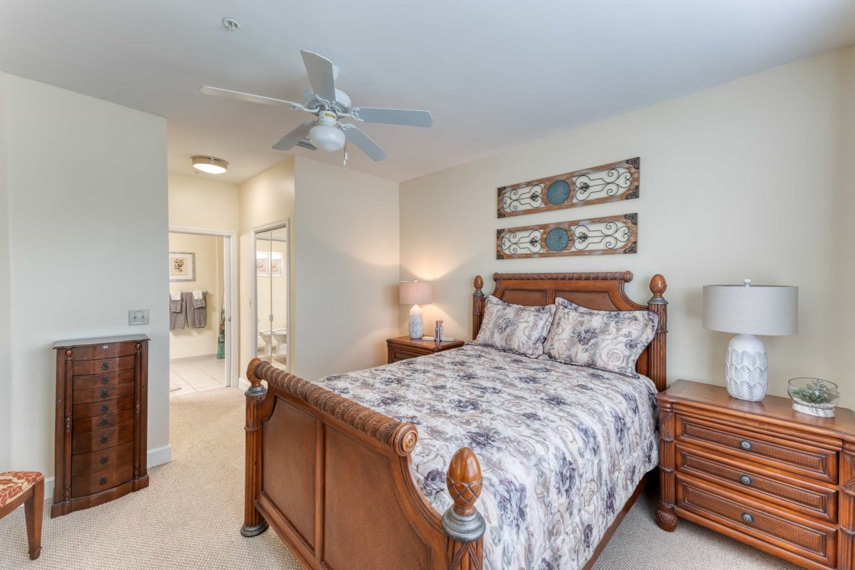 A cozy bedroom with a wooden bed frame, floral bedding, and matching bedside tables under artwork and a ceiling fan.