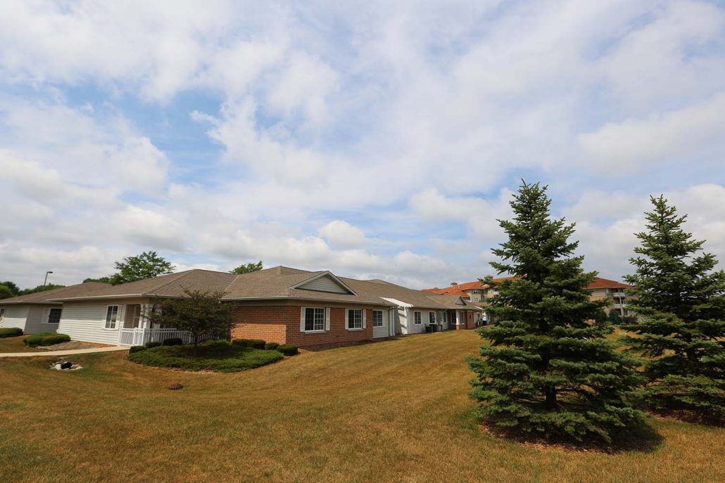 A suburban house with a large grassy yard and scattered trees under a cloudy sky.