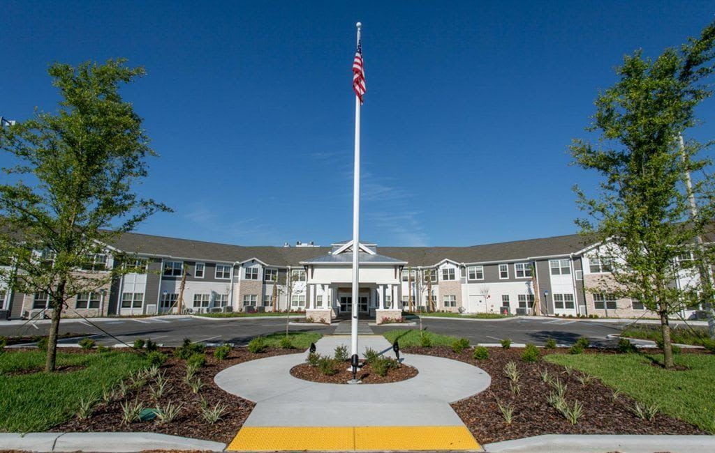 A modern building with a central entrance and an American flag on a flagpole surrounded by landscaping.