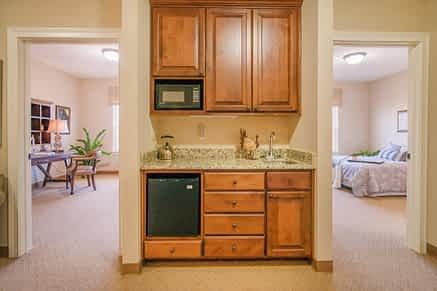 A compact kitchenette with wooden cabinets, featuring a microwave, sink, and small fridge.