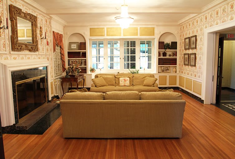 A cozy living room with a sofa facing a fireplace, surrounded by bookshelves and decorated walls.