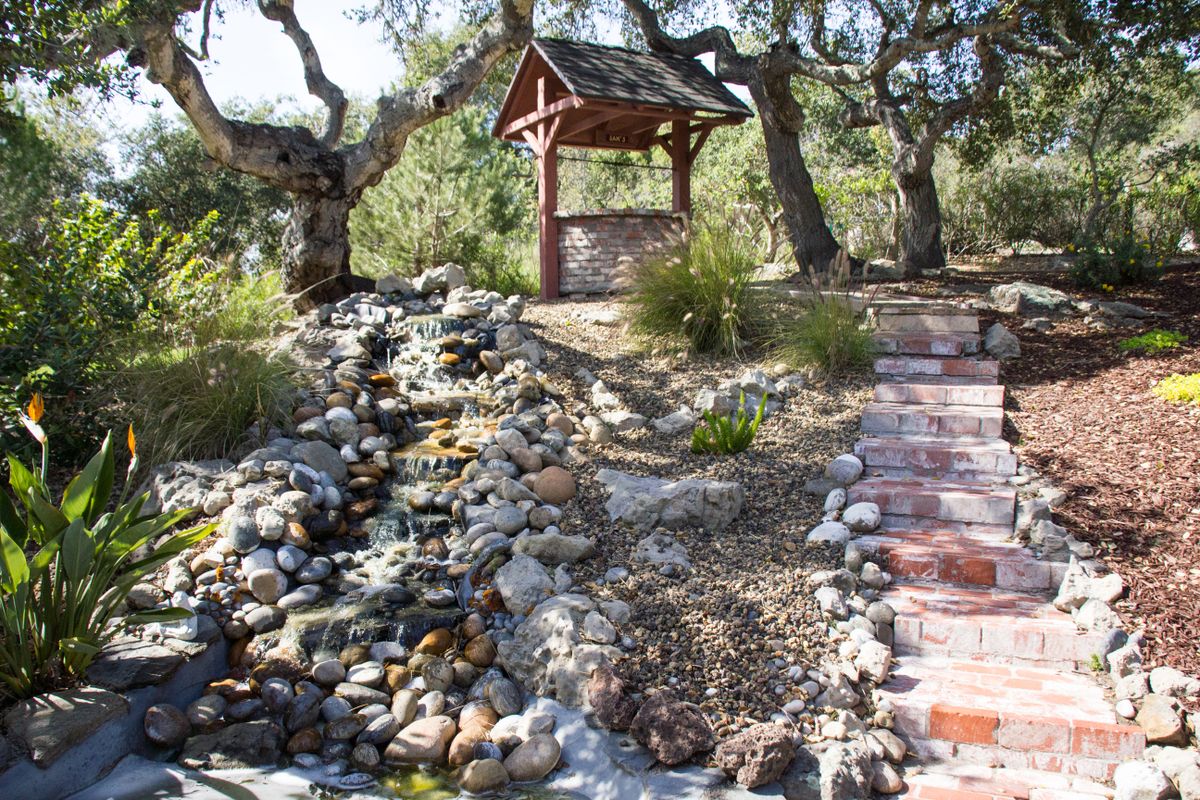 A tranquil garden scene featuring a stone path, a rustic well, and surrounding greenery.