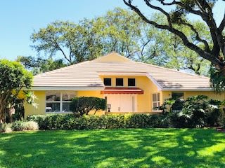 A charming yellow house surrounded by lush greenery in a suburban setting.