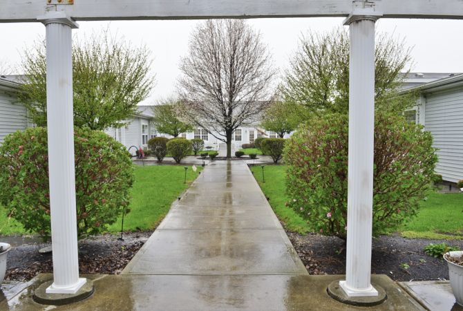 A wet pathway beneath an archway leads through a garden area with trees and bushes.