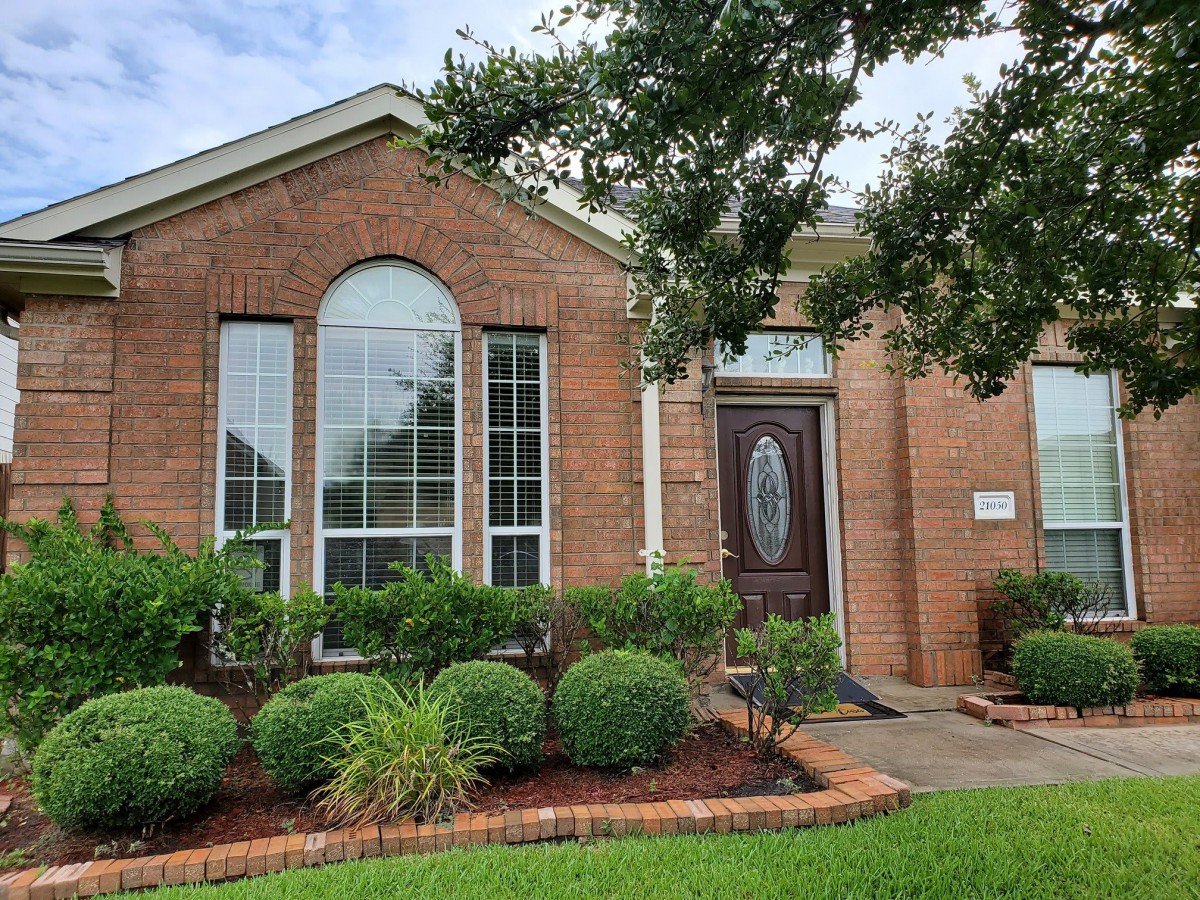 A brick house with a manicured front yard featuring shrubs and a tree.