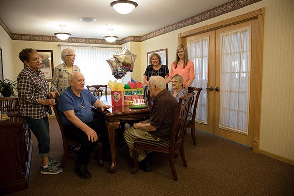 A group of people celebrating a birthday with gifts and balloons around a table.