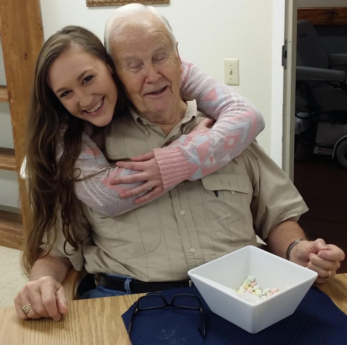 A young woman happily hugging an elderly man while sitting together at a table.