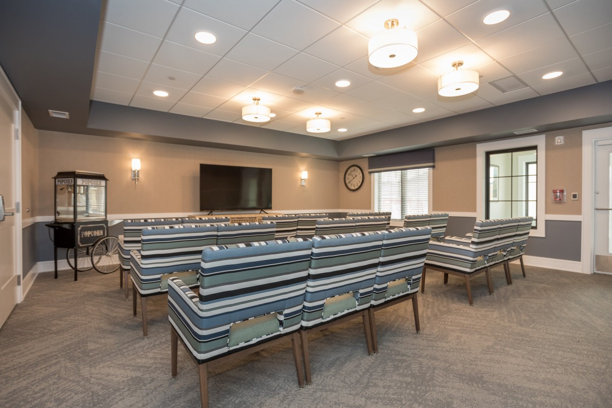 An empty classroom with rows of benches and desks, featuring overhead lighting and a television on the wall.