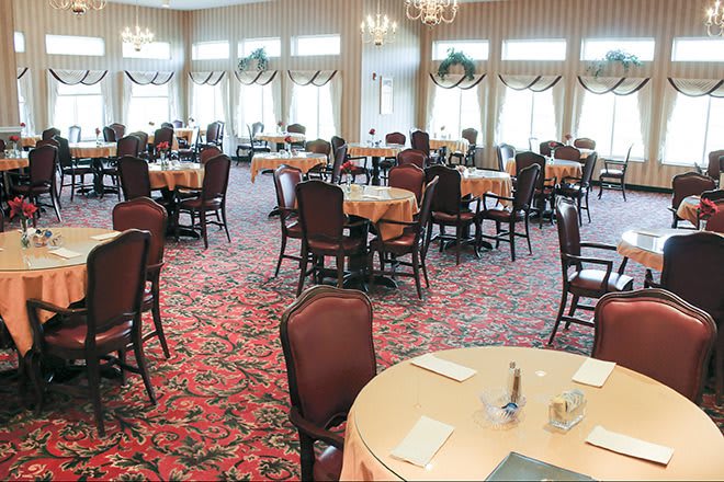 An elegant and formal dining room with neatly arranged tables and chairs, featuring a patterned carpet.