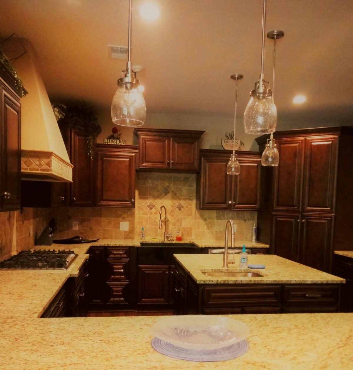 A modern kitchen with dark wood cabinets and granite countertops, illuminated by pendant lights.