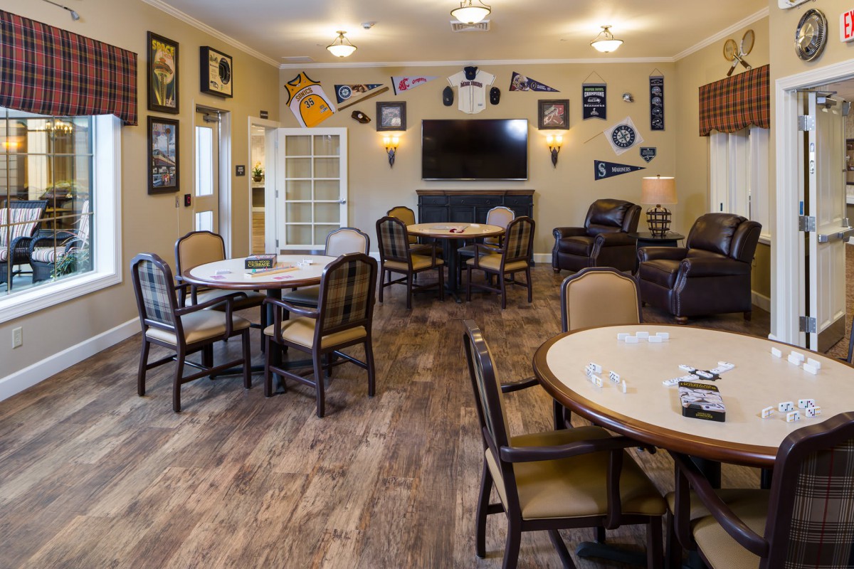 A cozy recreation room with tables, chairs, and a large television, decorated with various wall memorabilia.