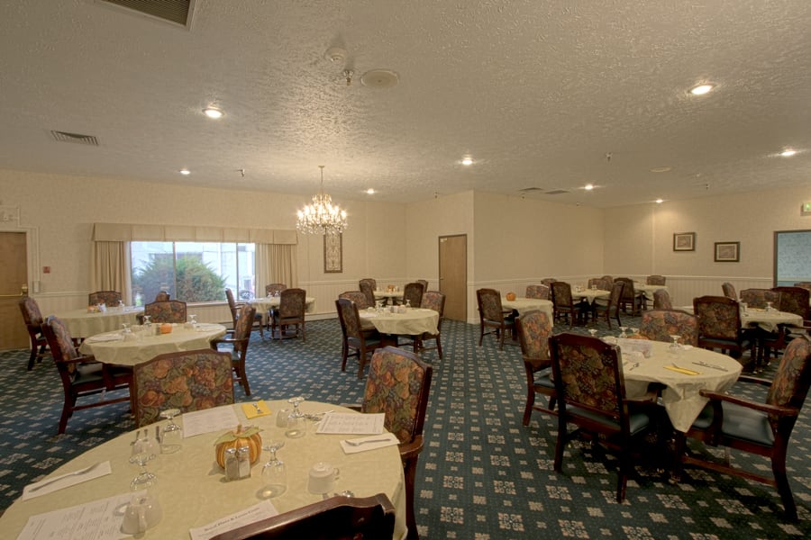 A spacious dining room with elegantly set tables and classic wooden chairs.
