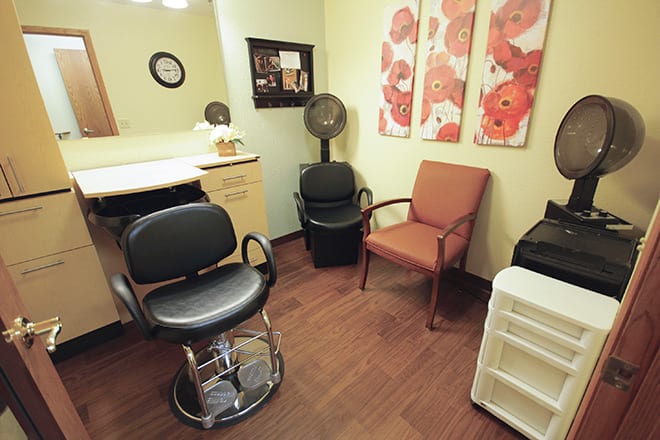 A cozy hair salon room with chairs, a hair dryer, and decorative art on the walls.