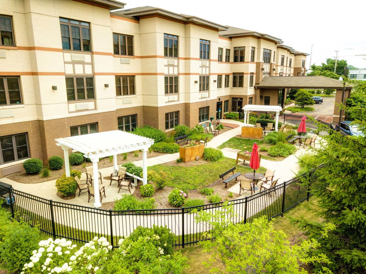 A well-maintained garden area with pathways and benches in front of a multi-story building.