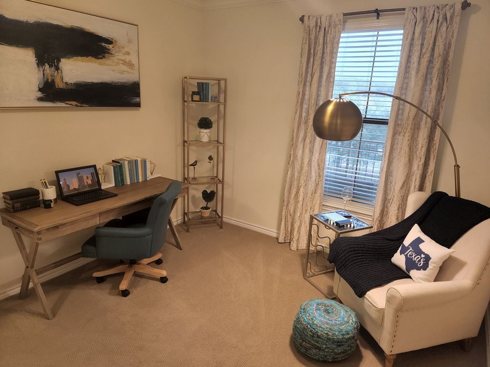 A cozy home office with a desk, armchair, and bookshelf near a window.
