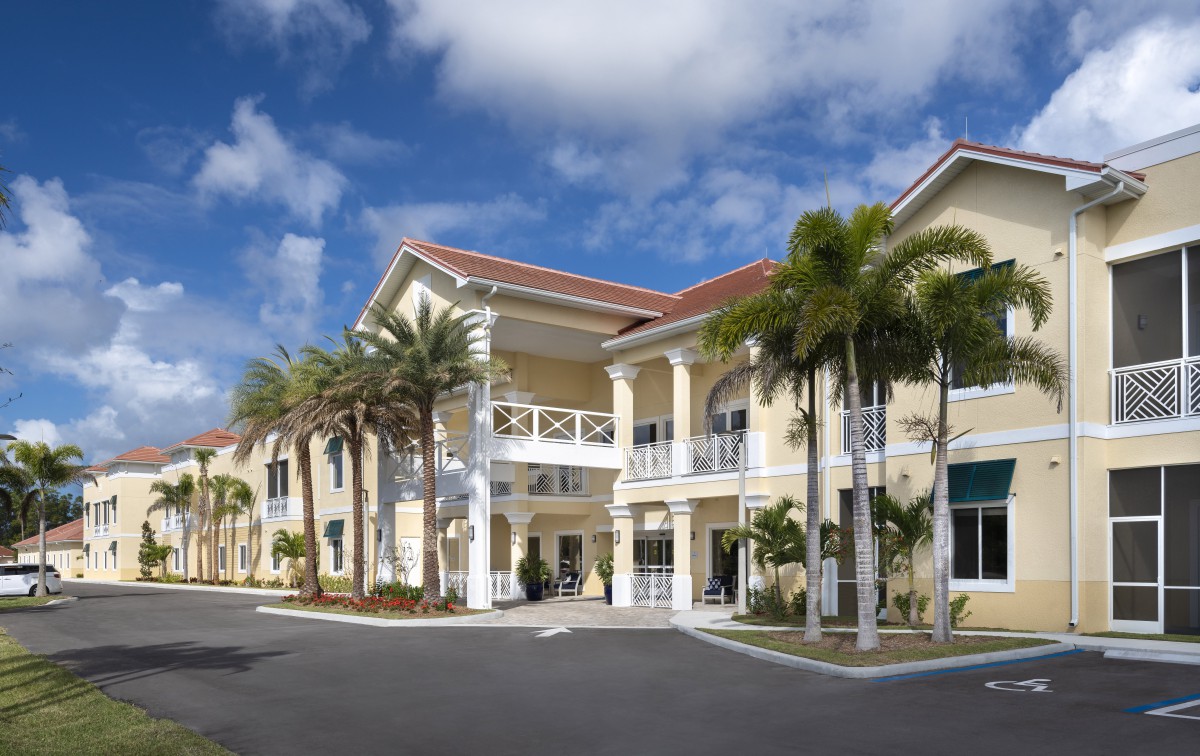 A two-story tropical building with palm trees under a cloudy sky.