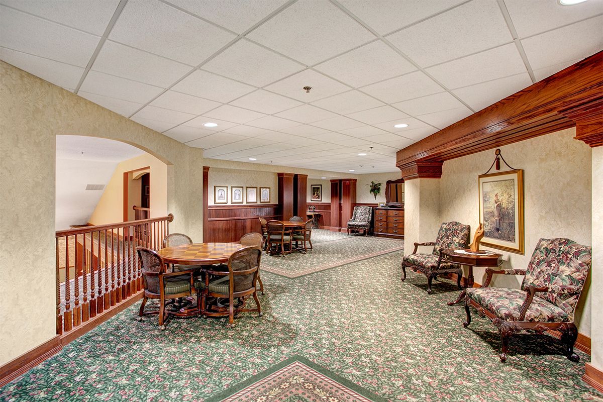 A spacious lounge area with tables and chairs, featuring wood paneling and carpet flooring.