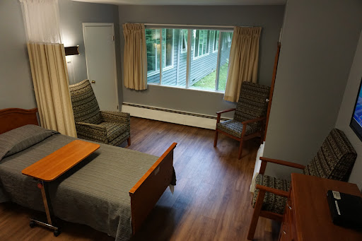 A cozy interior of a room featuring a bed, two chairs, and a large window with curtains.