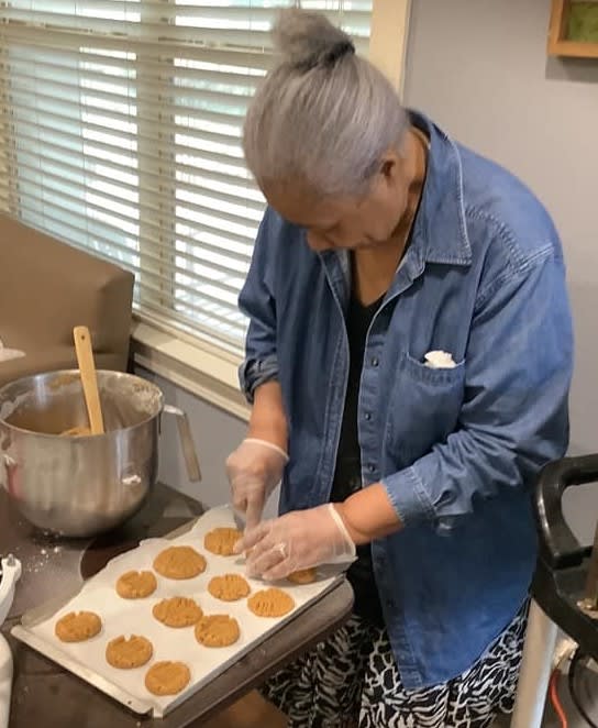 A person wearing a denim jacket prepares cookies on a baking sheet in the kitchen.