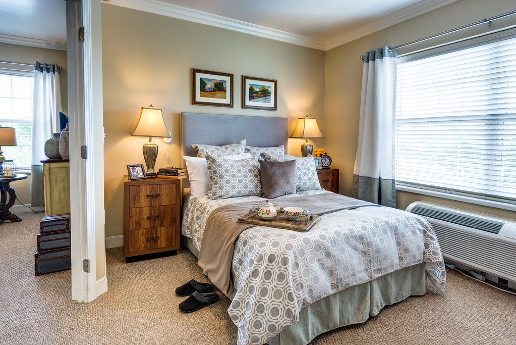 A cozy, well-decorated bedroom featuring a neatly made bed with patterned bedding, two nightstands with lamps, and a window letting in natural light.