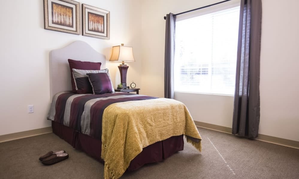 A cozy bedroom with a single bed, vibrant pillows, and a warm blanket next to a window with curtains.