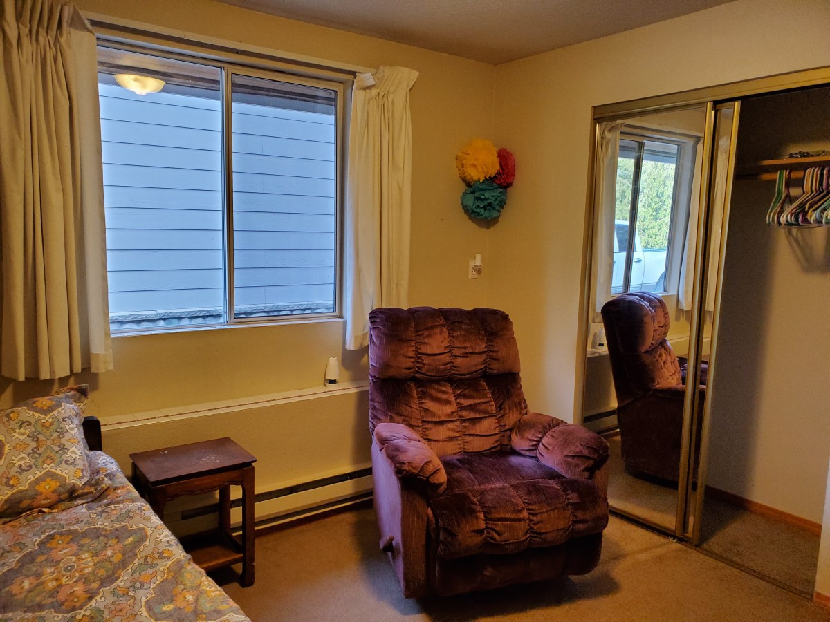 A cozy bedroom corner with a recliner, nightstand, and mirrored closet doors.