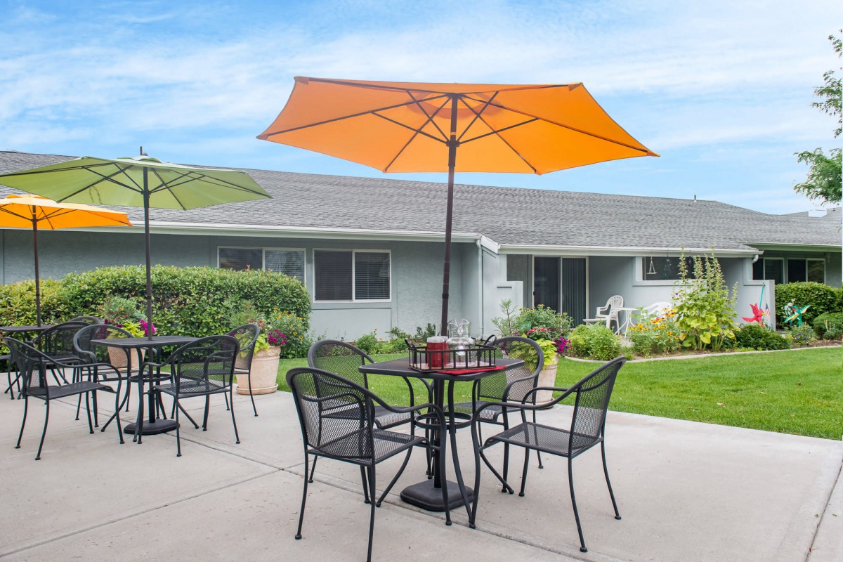 A patio with tables and chairs under orange umbrellas in a garden setting.