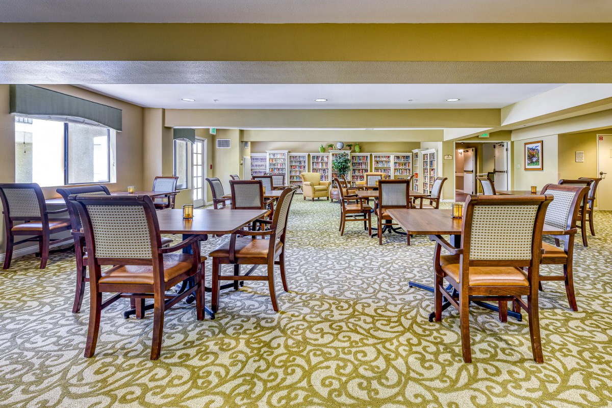 A well-lit dining area with arranged tables and chairs, featuring a patterned carpet.