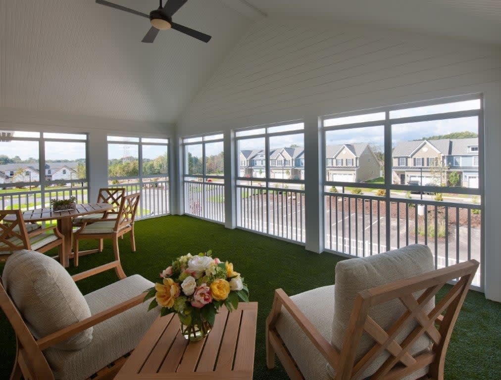 A bright sunroom with comfortable seating, a table adorned with flowers, and expansive windows offering a scenic view.
