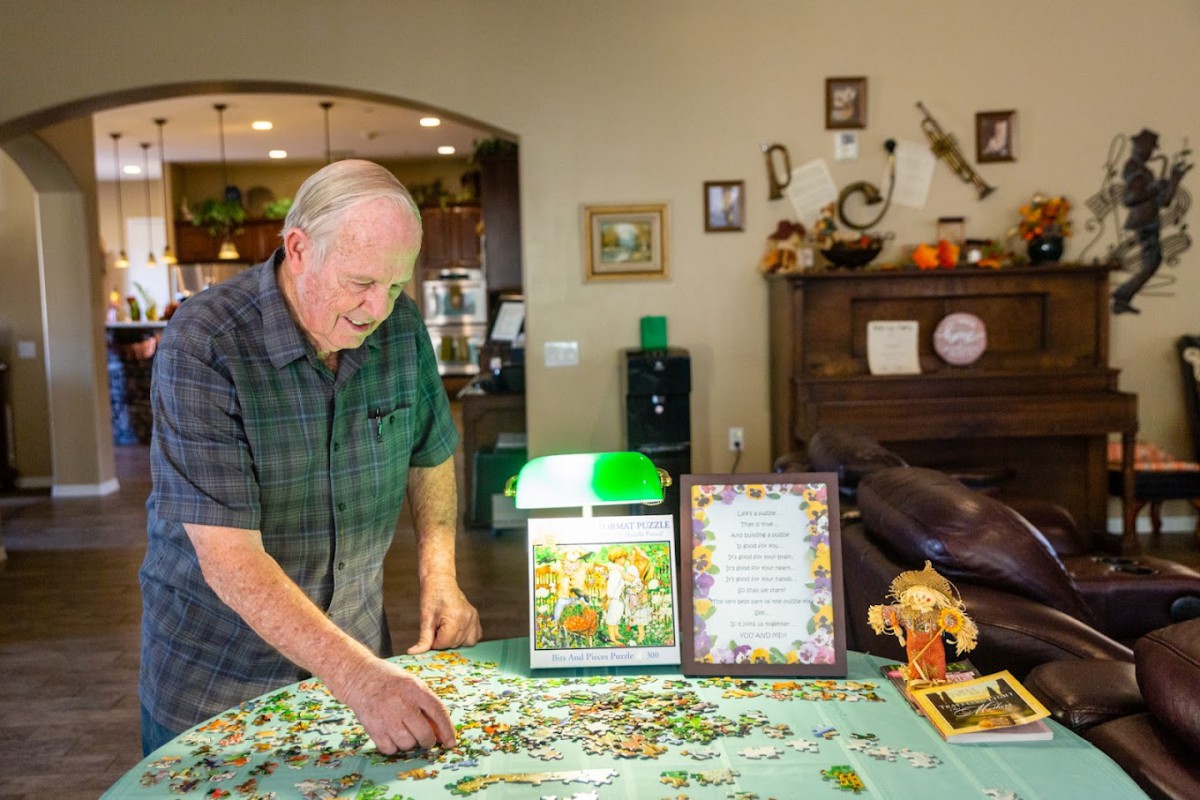 An elderly man working on a jigsaw puzzle at home.