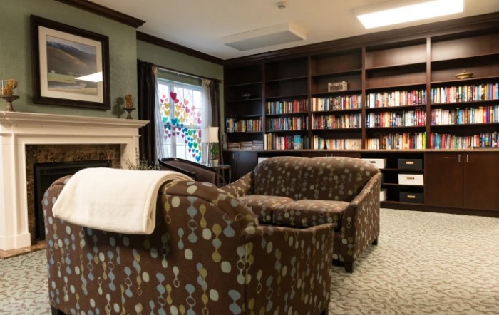 A cozy library reading room featuring comfortable armchairs, a fireplace, and shelves filled with books.