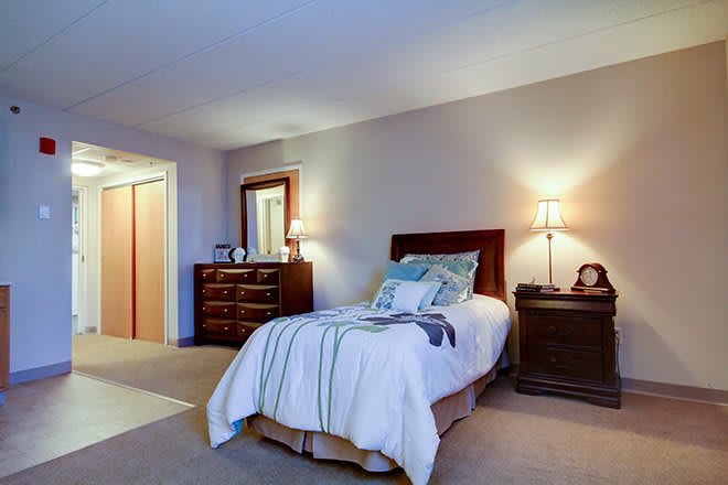 A cozy bedroom with a neatly made bed, wooden furniture, and warm lighting.