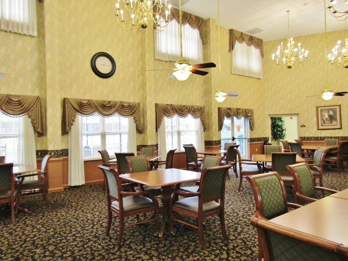 A well-lit dining room with elegant chandeliers and neatly arranged tables and chairs.