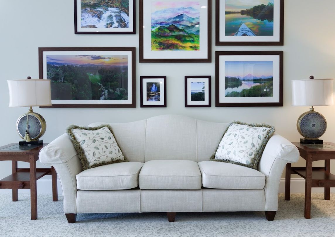 A cozy living room with a white sofa adorned with patterned cushions and a wall decorated with various landscape paintings.