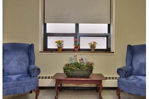 A cozy sitting area with two blue chairs flanking a small wooden table adorned with potted plants, set against a window backdrop.