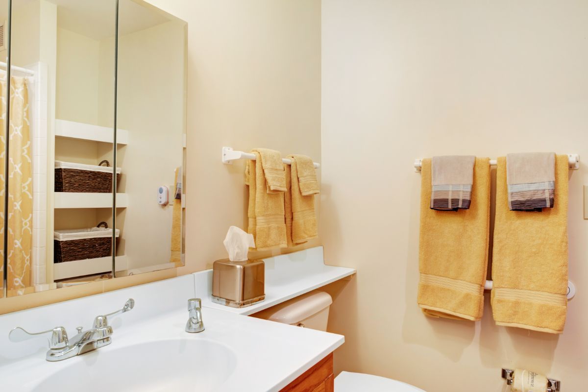 A tidy bathroom with yellow towels and a large mirror above the sink.