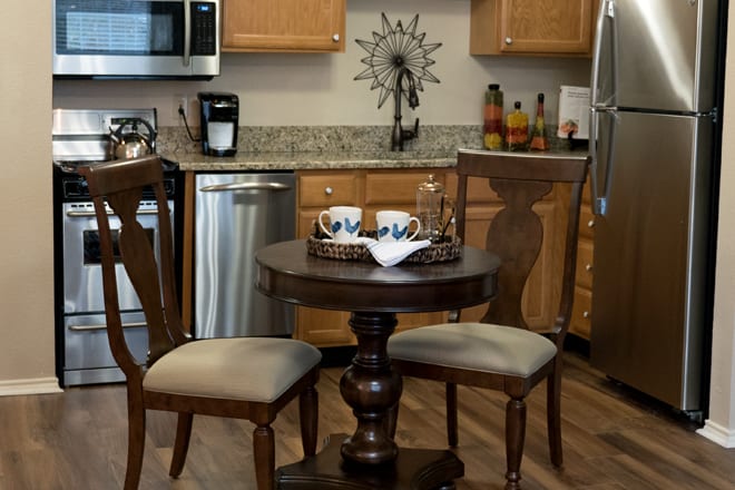 A cozy kitchen with a small wooden table and two chairs, surrounded by modern appliances and wooden cabinets.