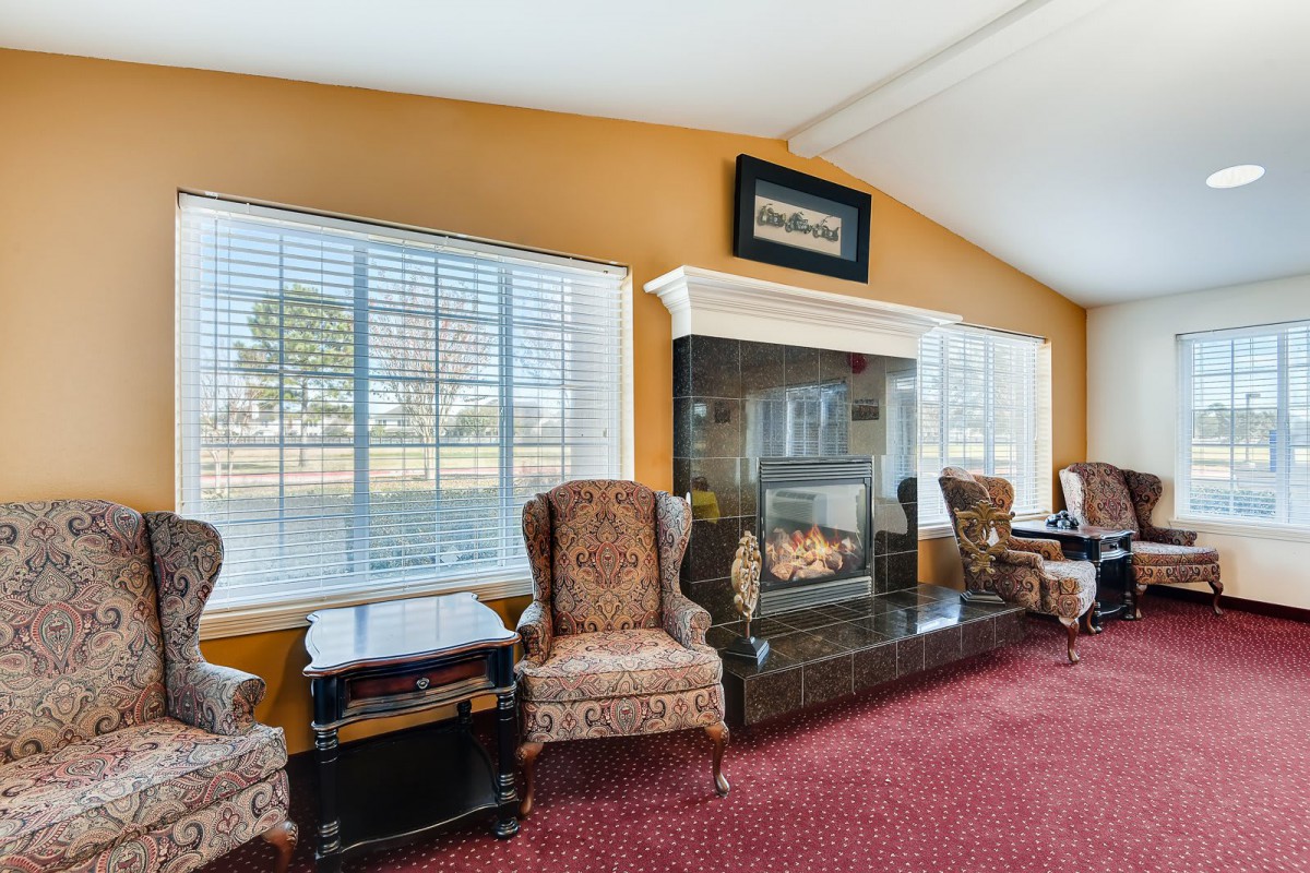A cozy living room featuring armchairs by a fireplace with large windows.