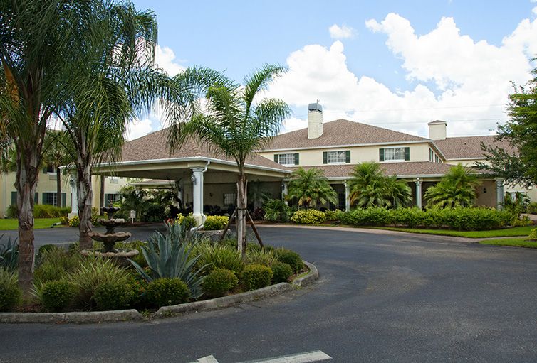 A hotel surrounded by palm trees with a circular driveway under a cloudy sky.
