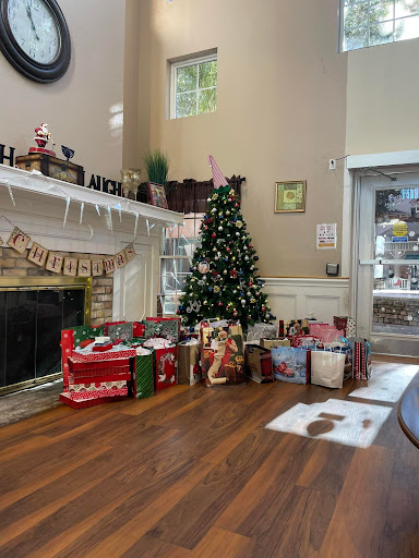 A cozy living room decorated for Christmas with a beautifully adorned tree and an array of gifts by the fireplace.