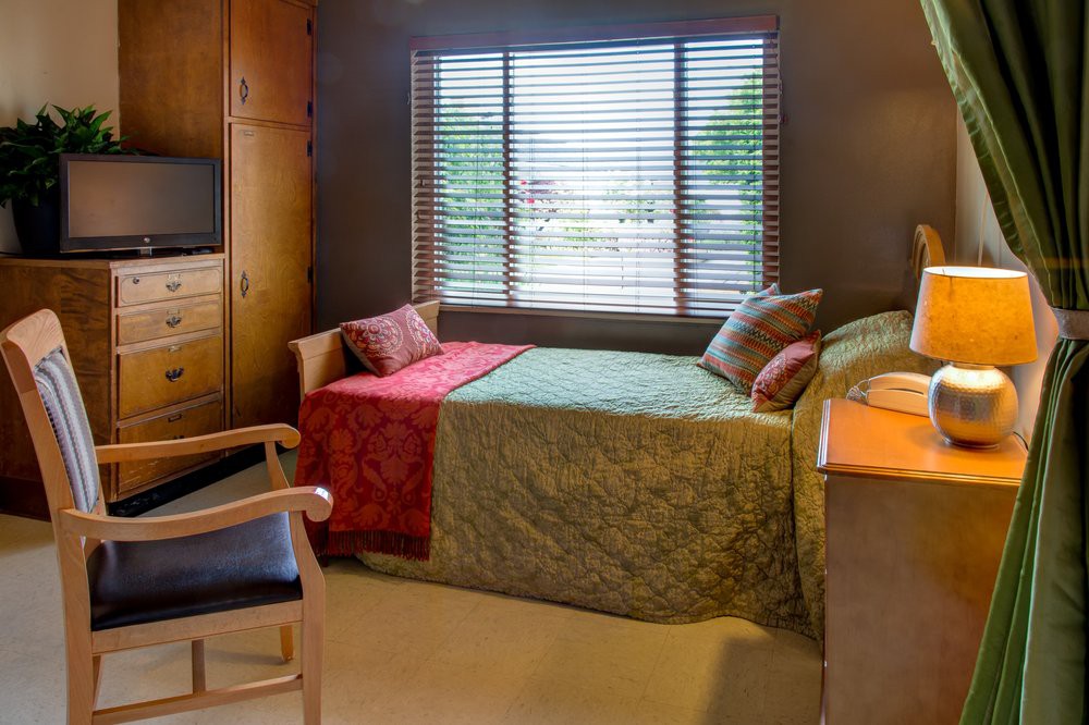A cozy bedroom with a single bed, colorful quilt, and window with blinds.