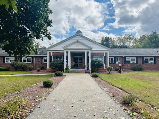 A welcoming entrance to a well-maintained building, surrounded by greenery and under a cloudy sky.