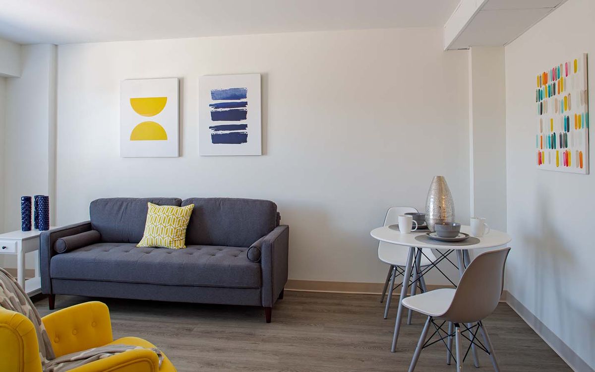 A modern living room with a gray sofa, colorful artwork, and a small dining area.