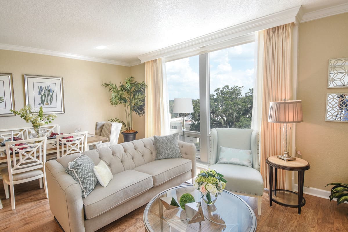 A bright and airy living room with modern decor, featuring a comfortable sofa, an armchair, a glass coffee table, and large windows allowing plenty of natural light.