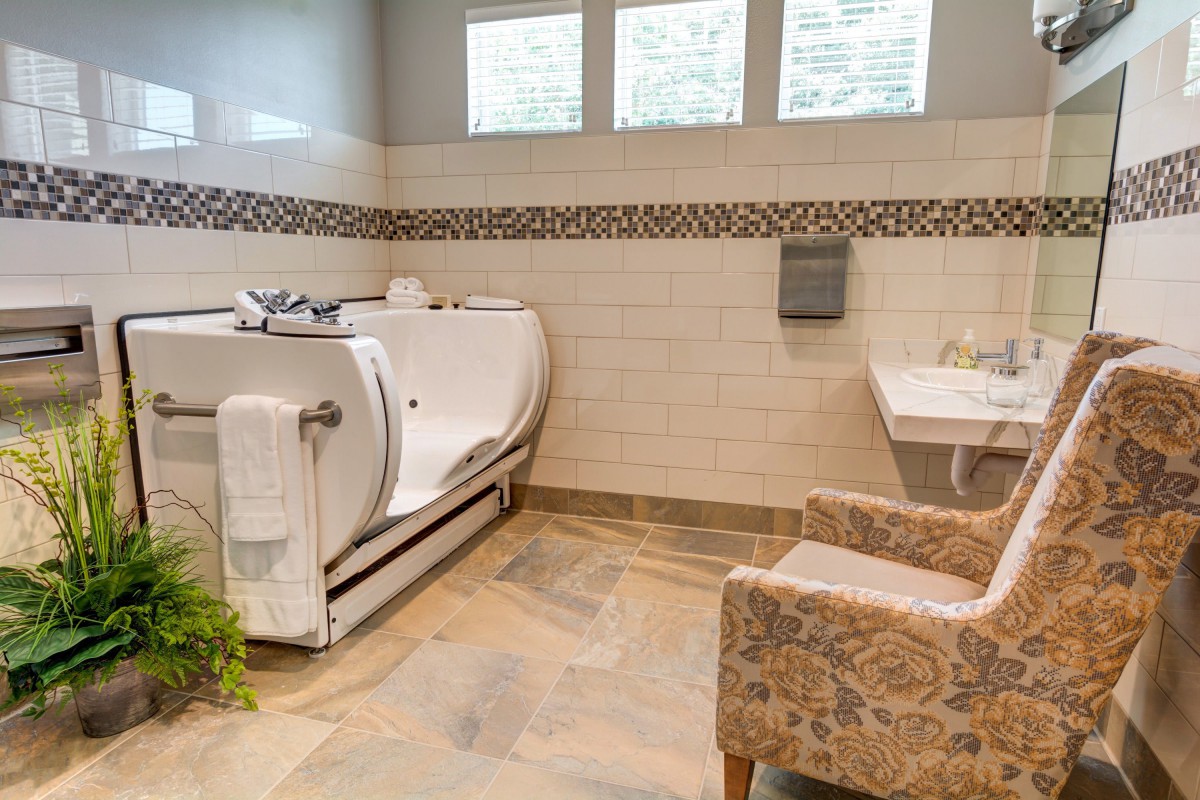 A bright and accessible bathroom featuring a walk-in tub, patterned tiles, and comfortable seating.