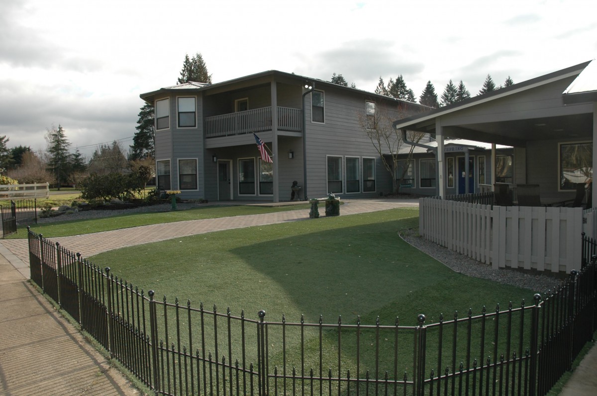 A residential apartment building with a well-maintained lawn and surrounding fence.